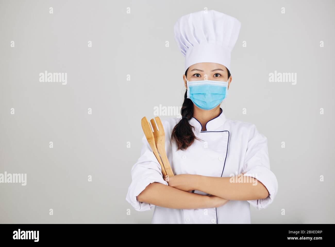 Confident young restaurant chef in medical mask posing with wooden utensils Stock Photo