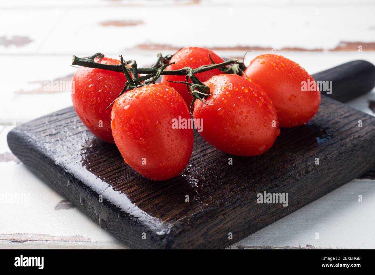 Ripe fresh cherry tomatoes on a branch on a wooden chopping Board ...