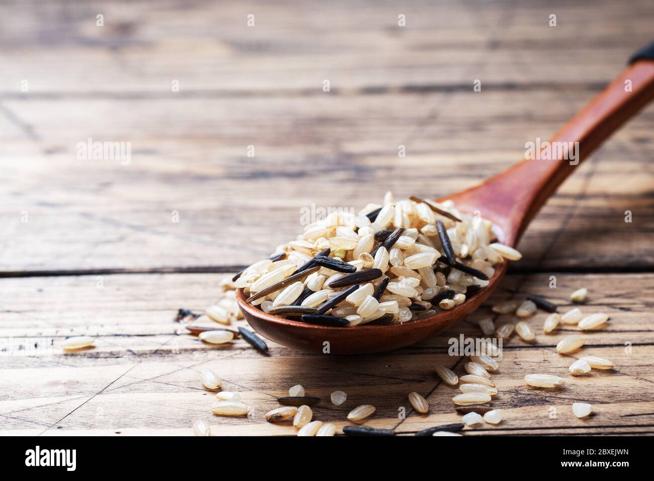 Raw wild rice in a wooden spoon. Raw rice grits on a wooden background. Copy space Stock Photo