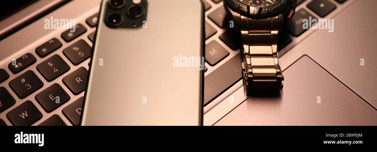 Silver smartphone and watch lie on laptop keyboard in office close-up Stock Photo