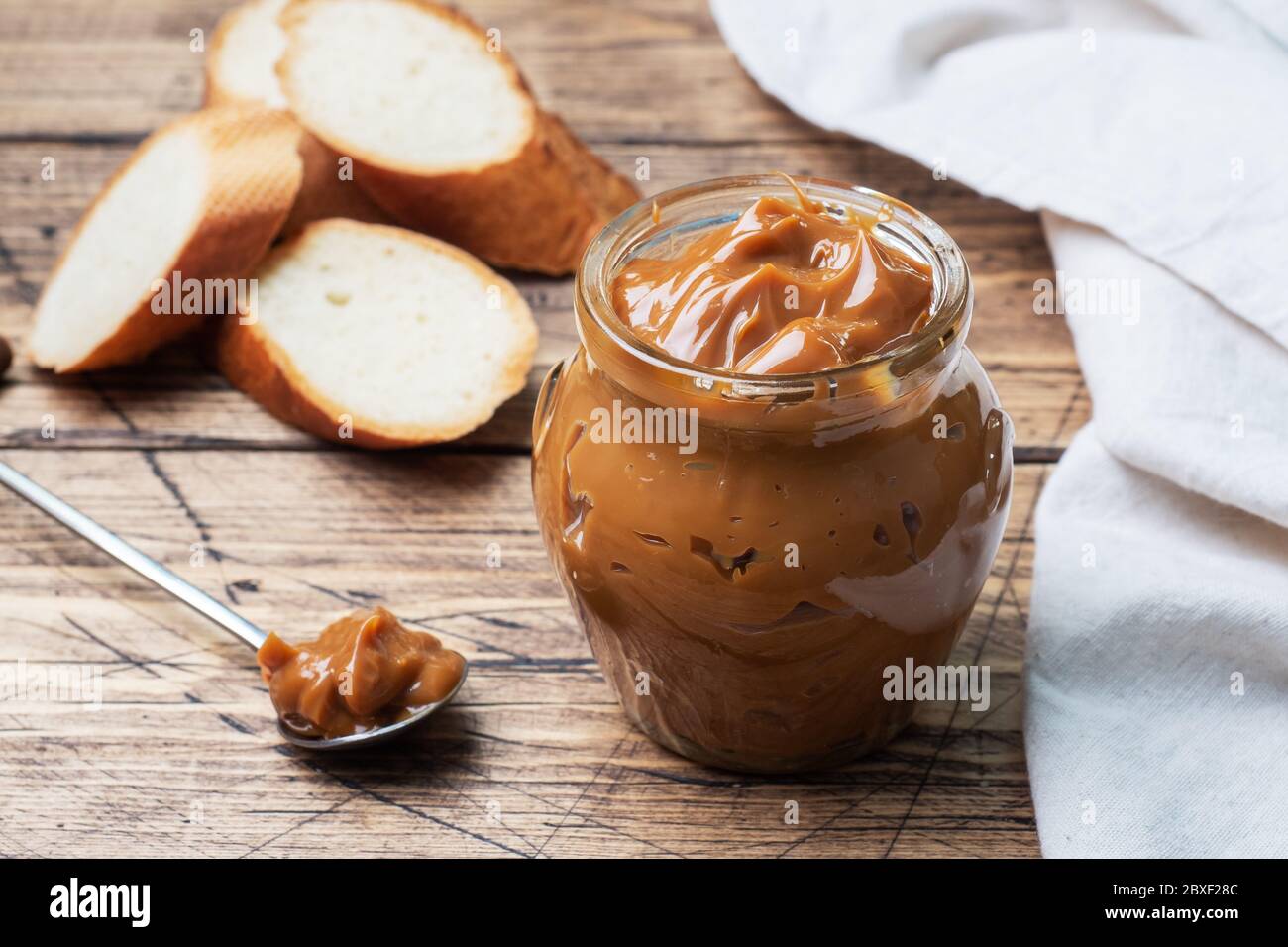 Boiled condensed milk with a glass jar on a wooden background. Sweet paste spread on slices of bread for Breakfast and dessert Stock Photo