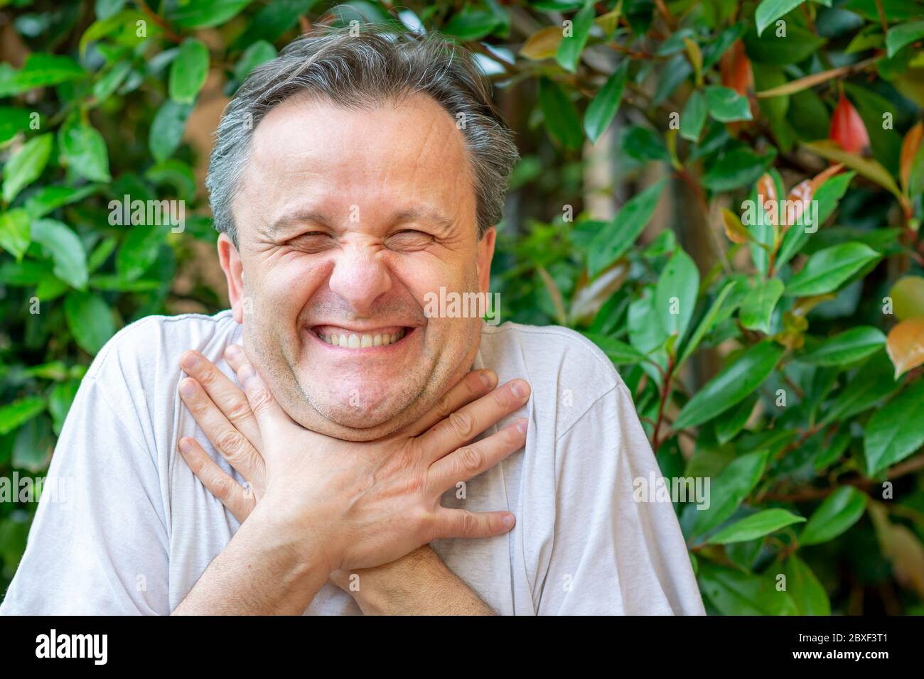 A white man makes a funny face while clutching his neck with his hands as if he wanted to choke Stock Photo