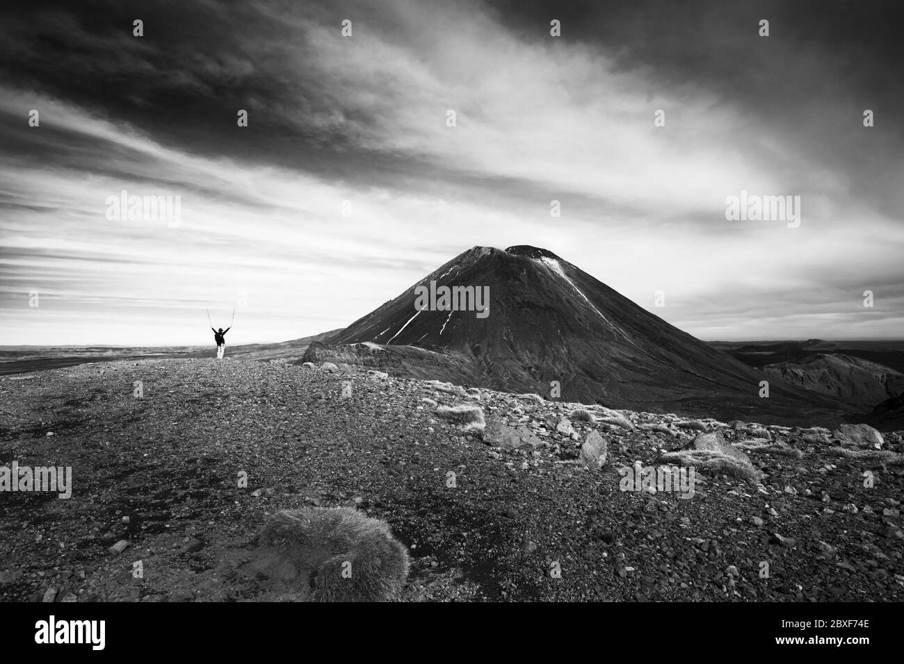 Black and white image of a lone tramper raising arms with the hiking poles, saluting to Mt Ngauruhoe on the Tongariro Alpine Crossing, New Zealand Stock Photo