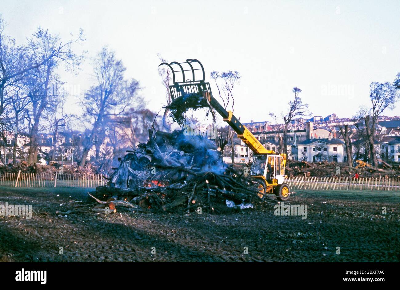 The aftermath of 'The Great Storm' in Brighton, East Sussex, England, UK – it occurred on the night of 15/16 October 1987. Here the big clean up is happening on 'The Level', an urban park in central Brighton. A JCB piles timber and debris on to a large bonfire on 'The Level', an urban park in central Brighton. 'The Great Storm' of 1987 was a violent tropical cyclone, with hurricane-force winds causing casualties and great damage in the UK and France. Stock Photo