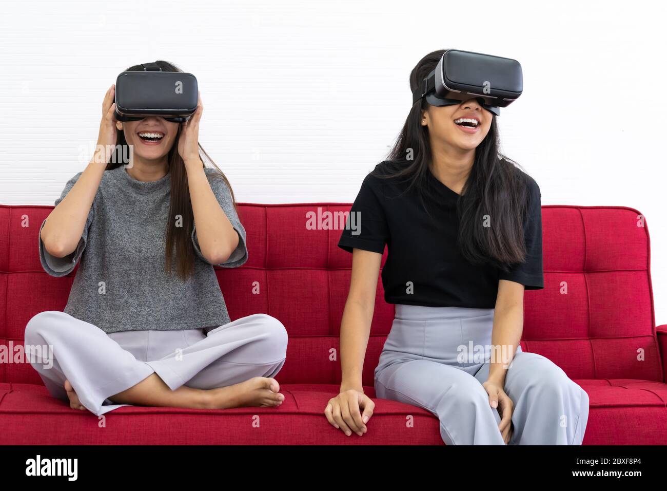 Two Asian beautiful women smiling during playing VR video games experience in living room house for good mental health while quarantine. Game technolo Stock Photo