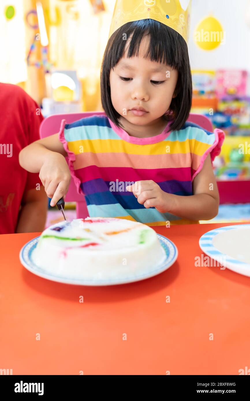 Asian girl kid cutting her birthday cake celebrate with mom alone because city lockdown while COVID-19 Pandemic. Celbration and quarantine concept. Stock Photo