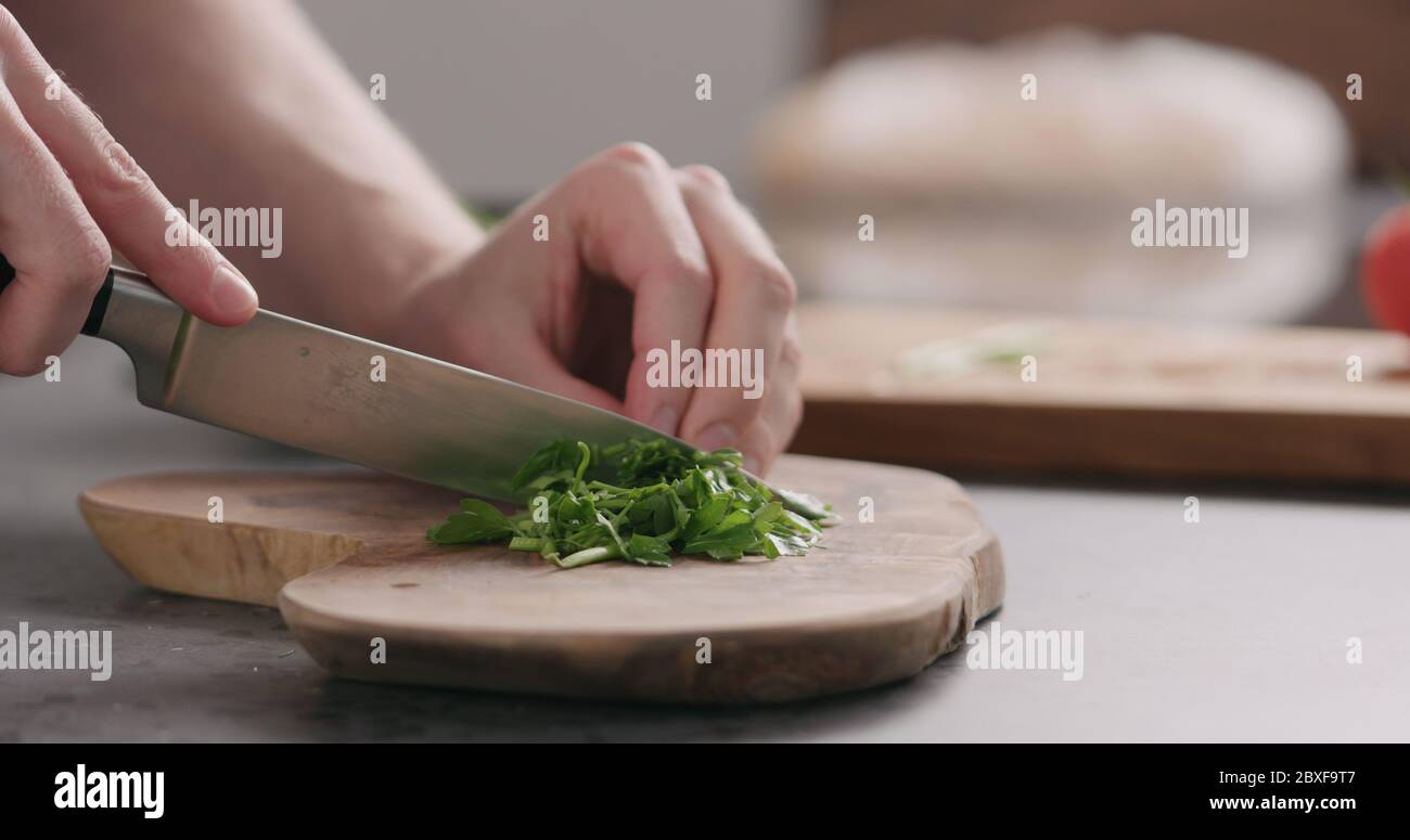 https://c8.alamy.com/comp/2BXF9T7/man-chopping-fresh-parsley-on-olive-board-side-view-2BXF9T7.jpg