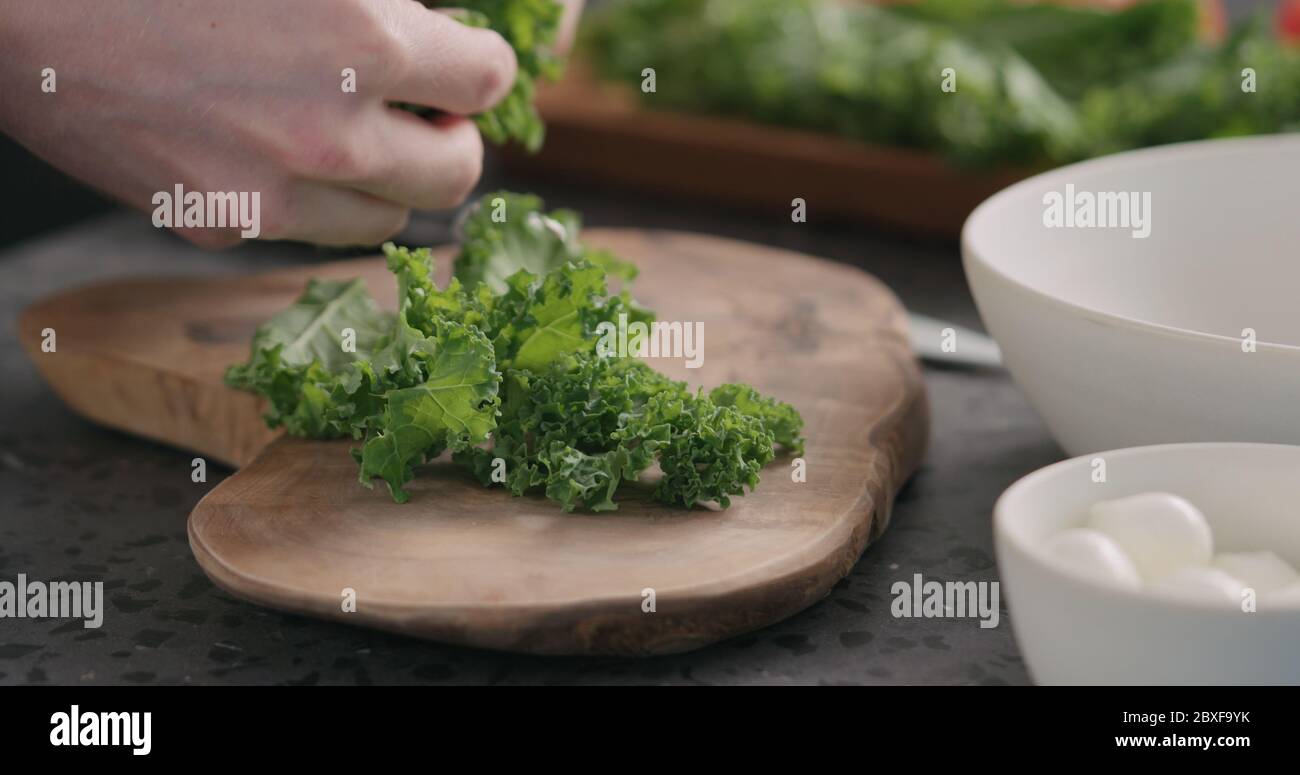 man tearing kale leaves to make it softer for salad on kitchen side view Stock Photo