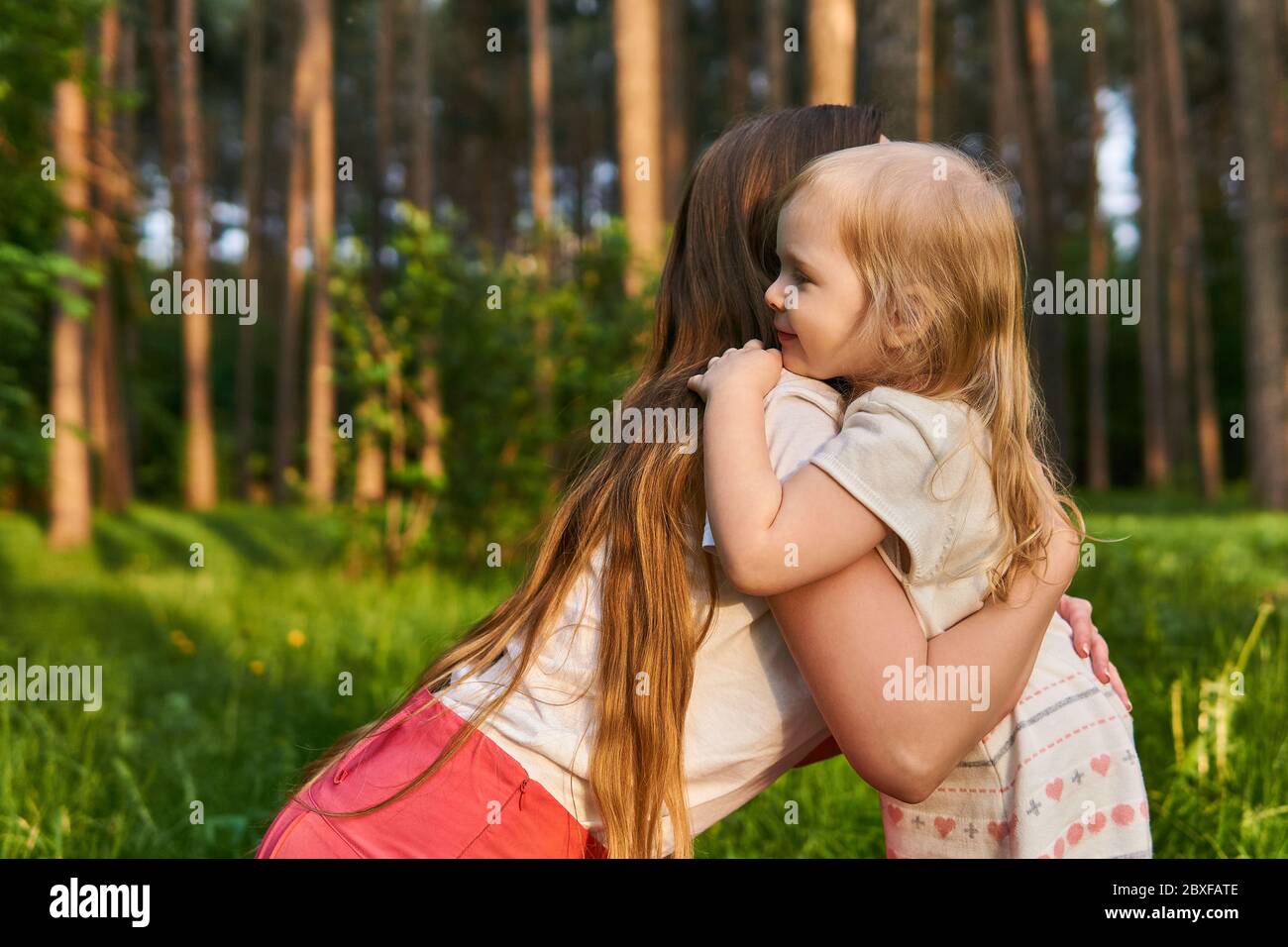 woman crouching affectionately hugs her toddler daughter outdoors in a park Stock Photo