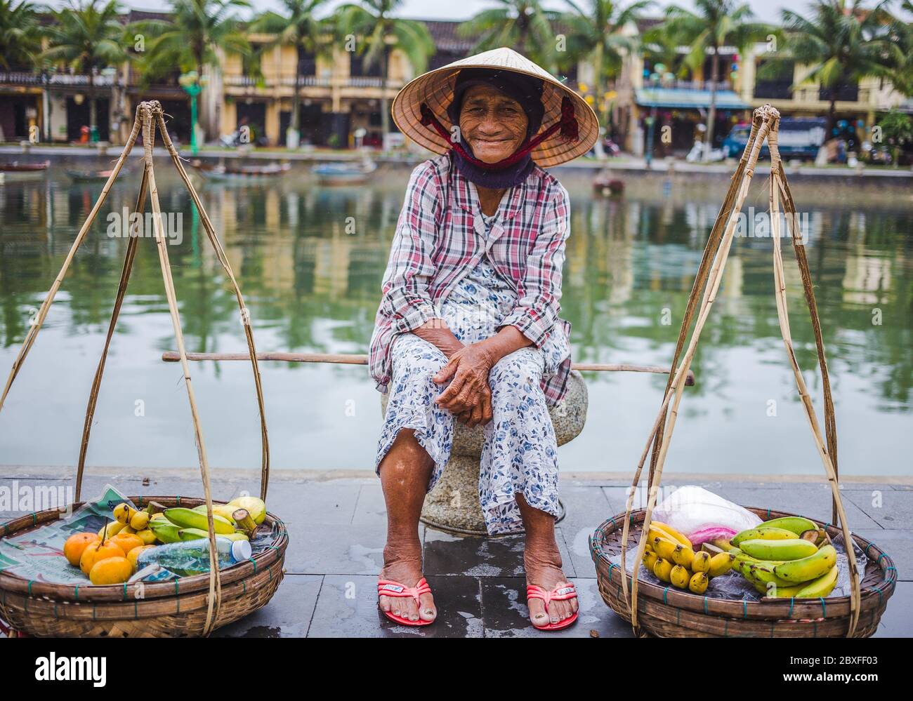 HOI AN, VIETNAM - 27TH MARCH 2017: An elderly lady waiting by the side of the river in Hoi An selling to sell fruit. Stock Photo