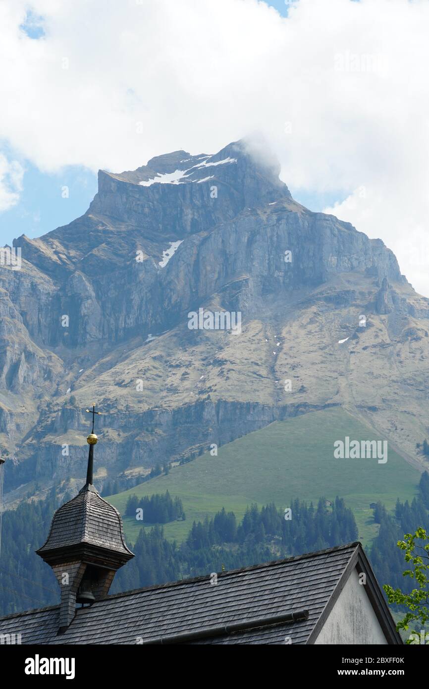 Mountain Hahnen in the springtime with the rests of snow and some clouds around it and bell tower of St. Jakob chapel. Stock Photo