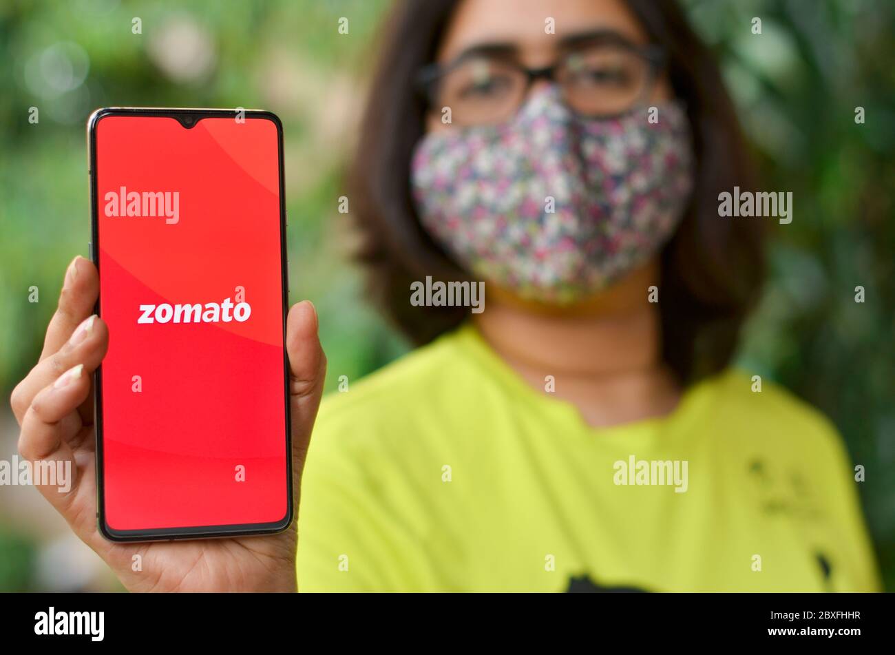 Mumbai, India, 2020. Girl wearing mask showing Zomato Food Delivery app on a mobile phone. During Corona Virus (Covid-19) disease pandemic lock down, Stock Photo