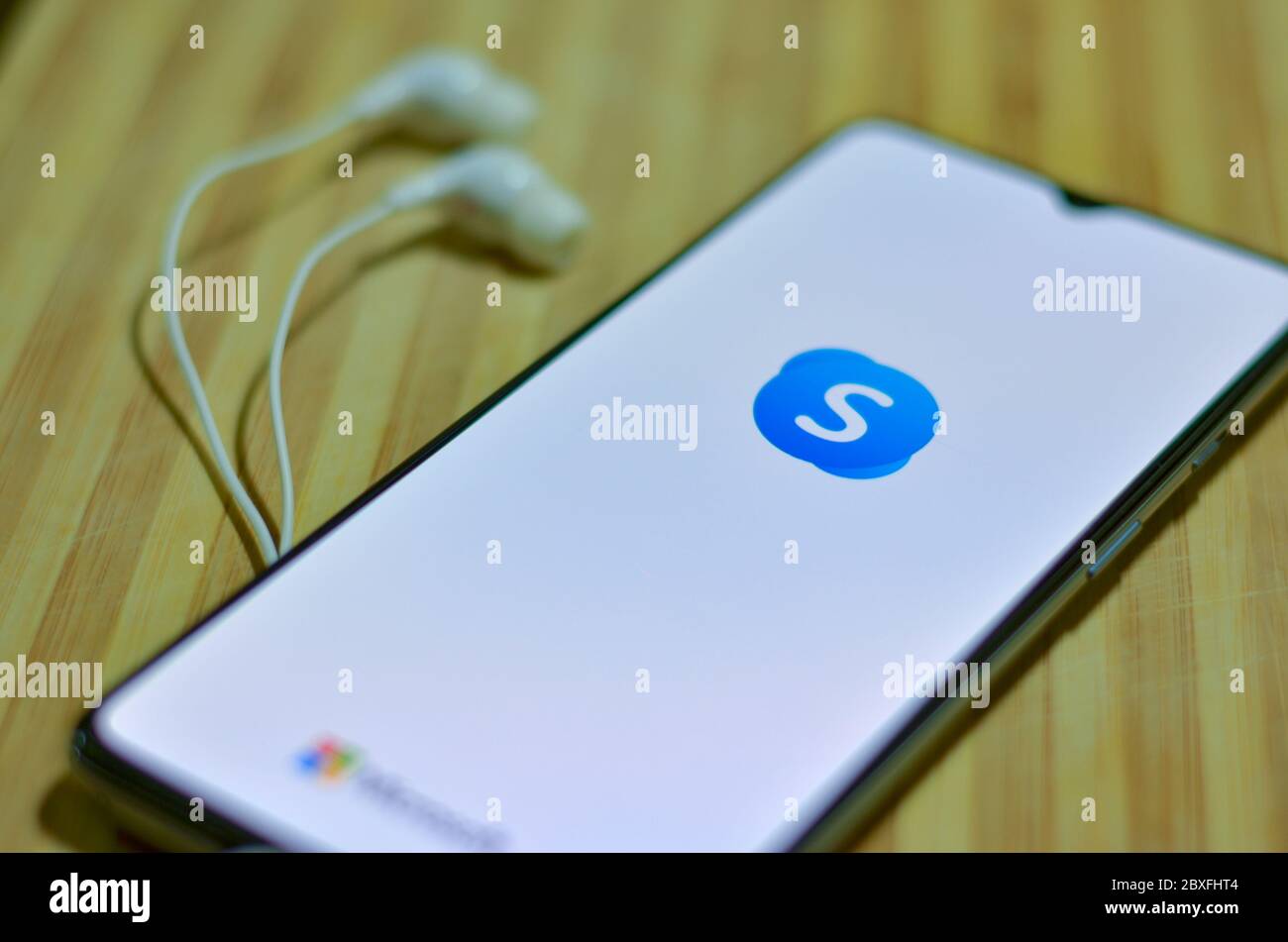 London, UK, 2020. Flat lay of Skype app icon on the smartphone screen on display and a pair of earphones on a wooden board background. SKype is a popu Stock Photo