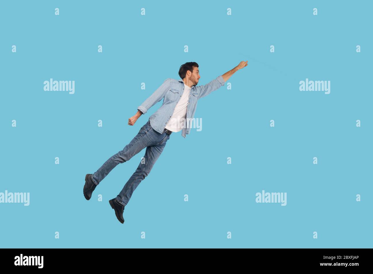 Full length portrait of man in denim outfit flying up as superhero with raised hand and inspired ambitious expression, achieving goal, jumping high in Stock Photo