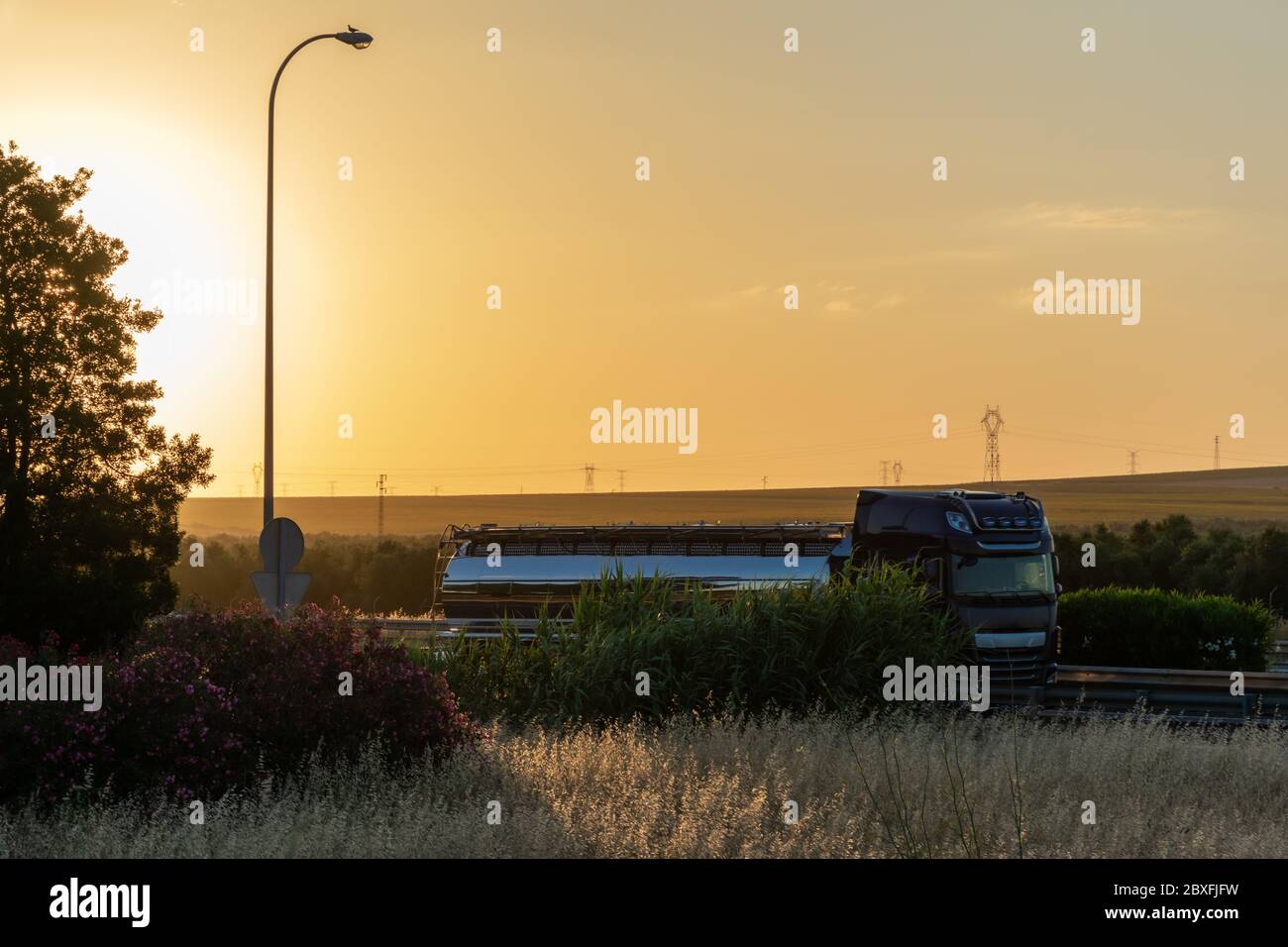 Steel tanker truck driving on the highway with a sunset sky Stock Photo