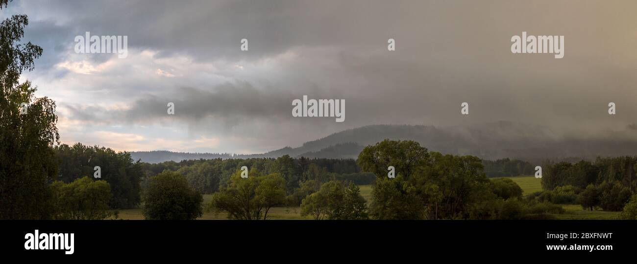 landscape with hills, forest and trees - rain, cloudy sky, partly shining blue sky Stock Photo