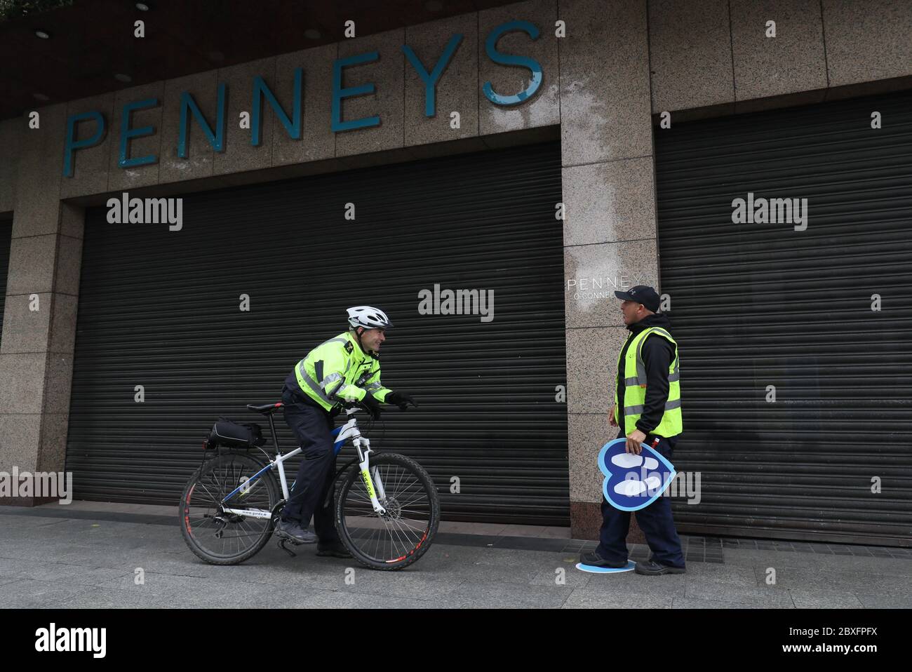 Garda sergeant Rodger Quinn (left) speaks to Dublin city council worker, Joe Carroll, putting down queue stickers on O'Connell Street, outside Penneys in Dublin, ahead of its reopening as phase two of the Ireland's coronavirus recovery road map will begin on Monday as planned, along with other measures originally envisaged for later phases. Stock Photo