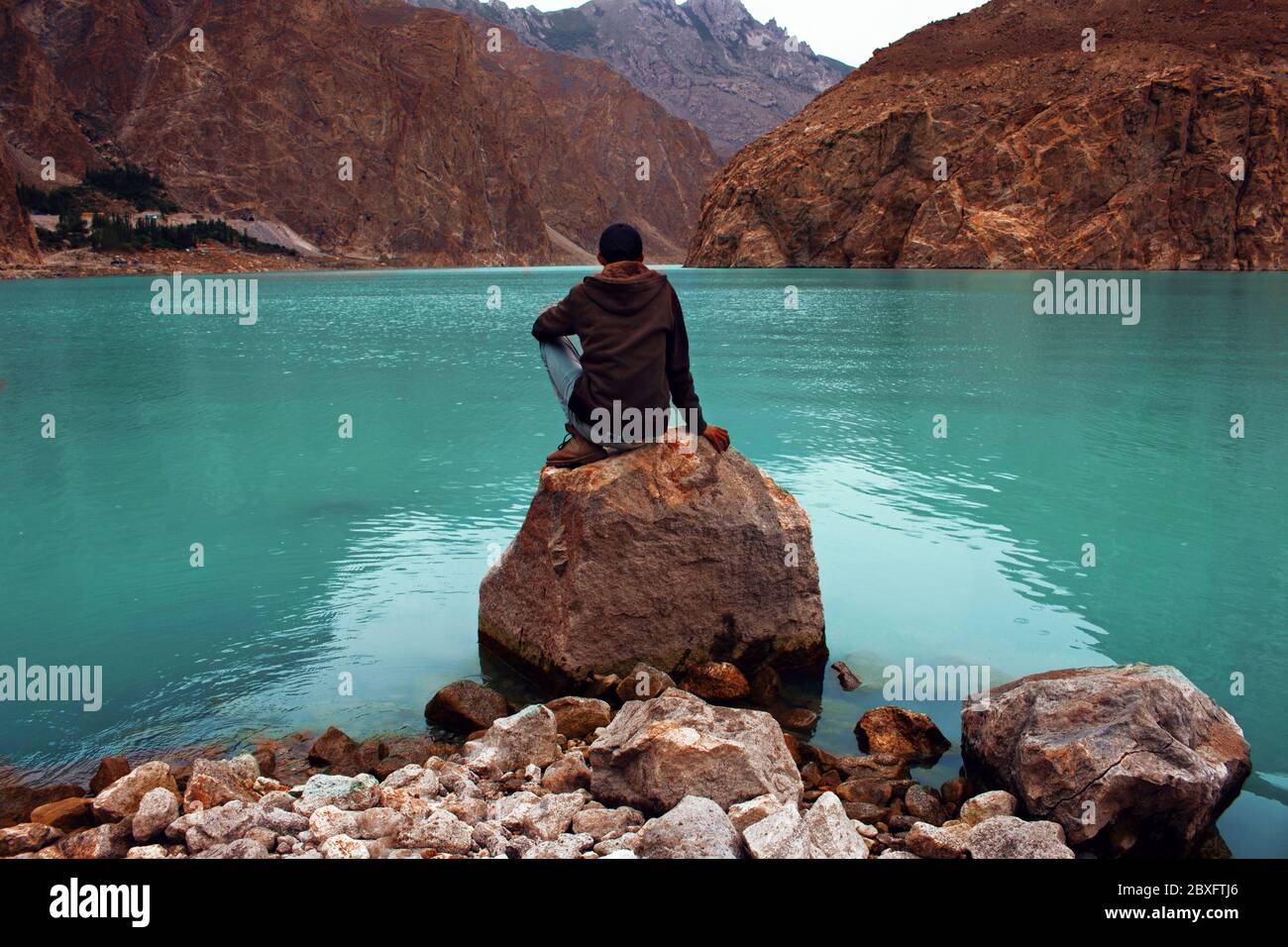 Men sitting on rock at Attabad Lake, Karakoram Highway, Hunza, Pakistan Stock Photo