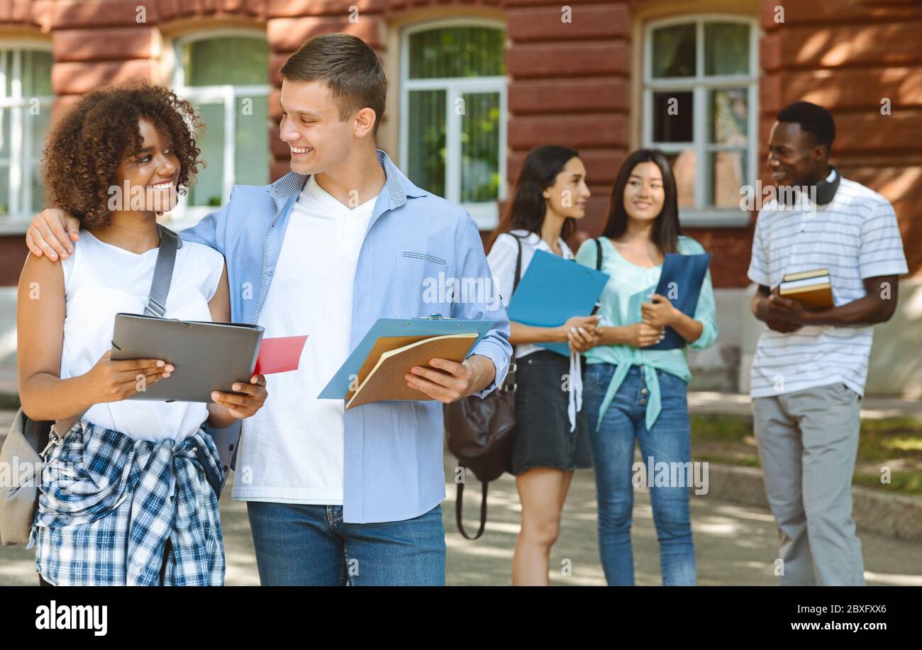 Smiling student cuddling his black girlfriend outdoors during break in classes Stock Photo