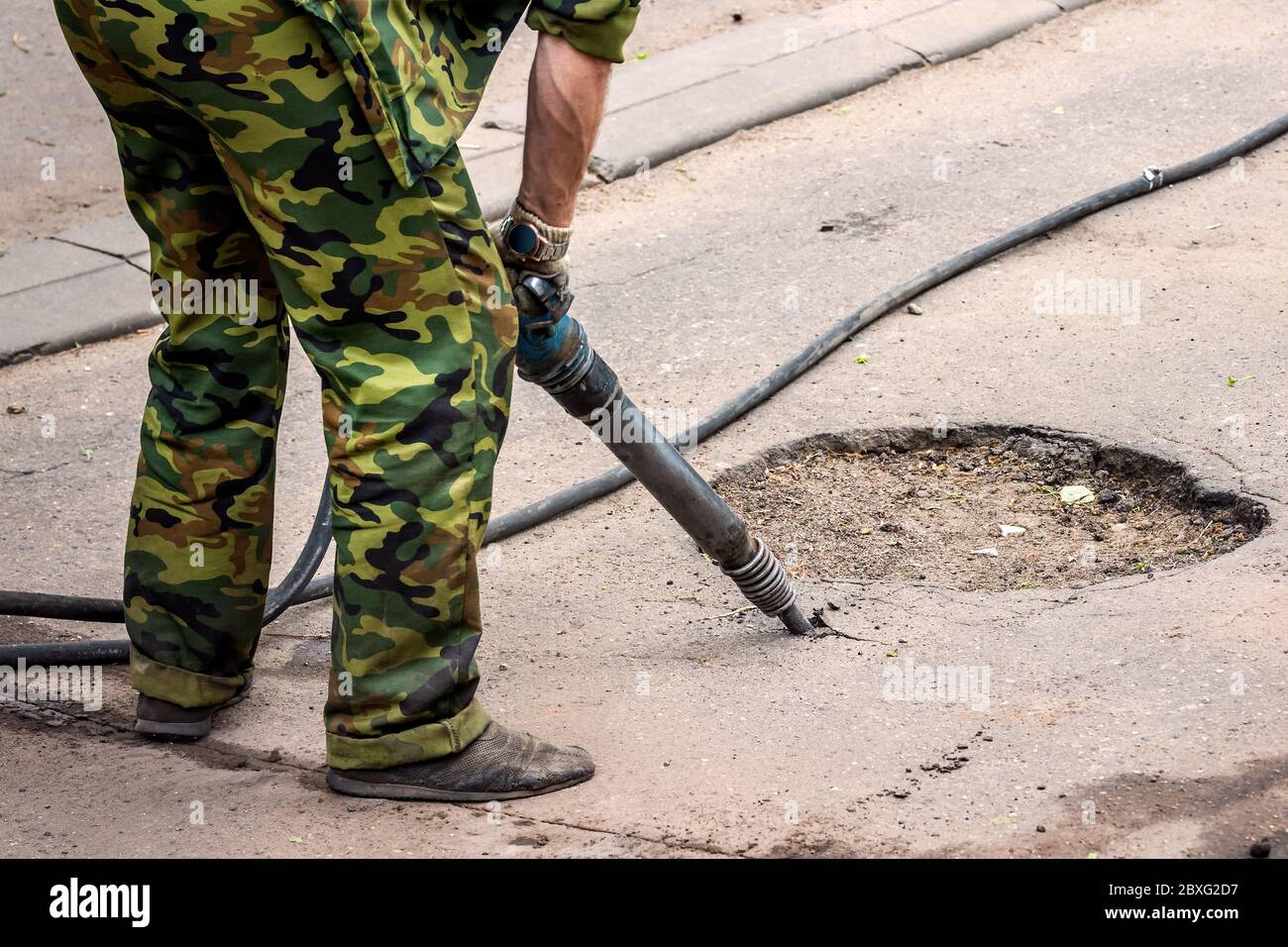 Worker in uniform repairing asphalt road with a jackhammer. Concept renovation, major repairs of the main street in city, road construction. Stock Photo