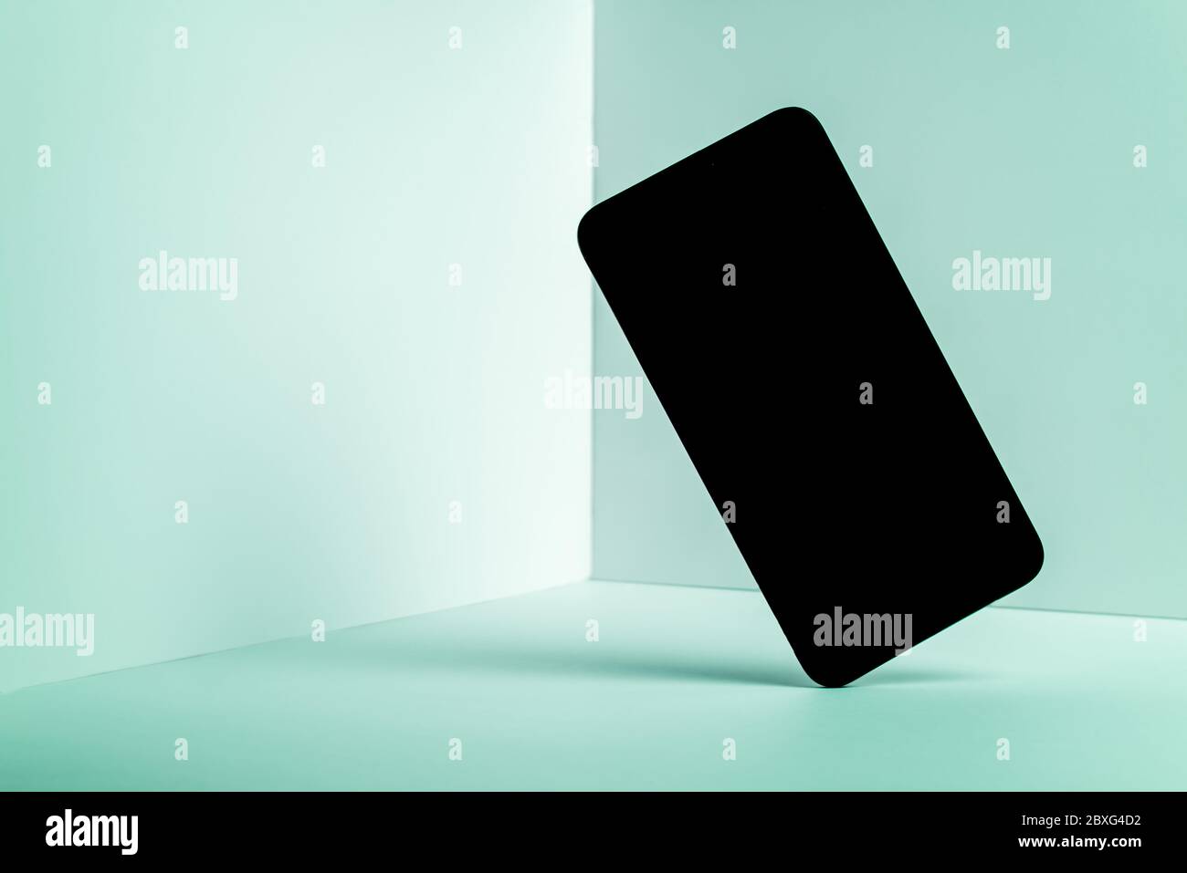 Minimalist modern smartphone mockup for presentation, in perspective front of the corner angle of the wall, with overlapping shadows on green backgrou Stock Photo