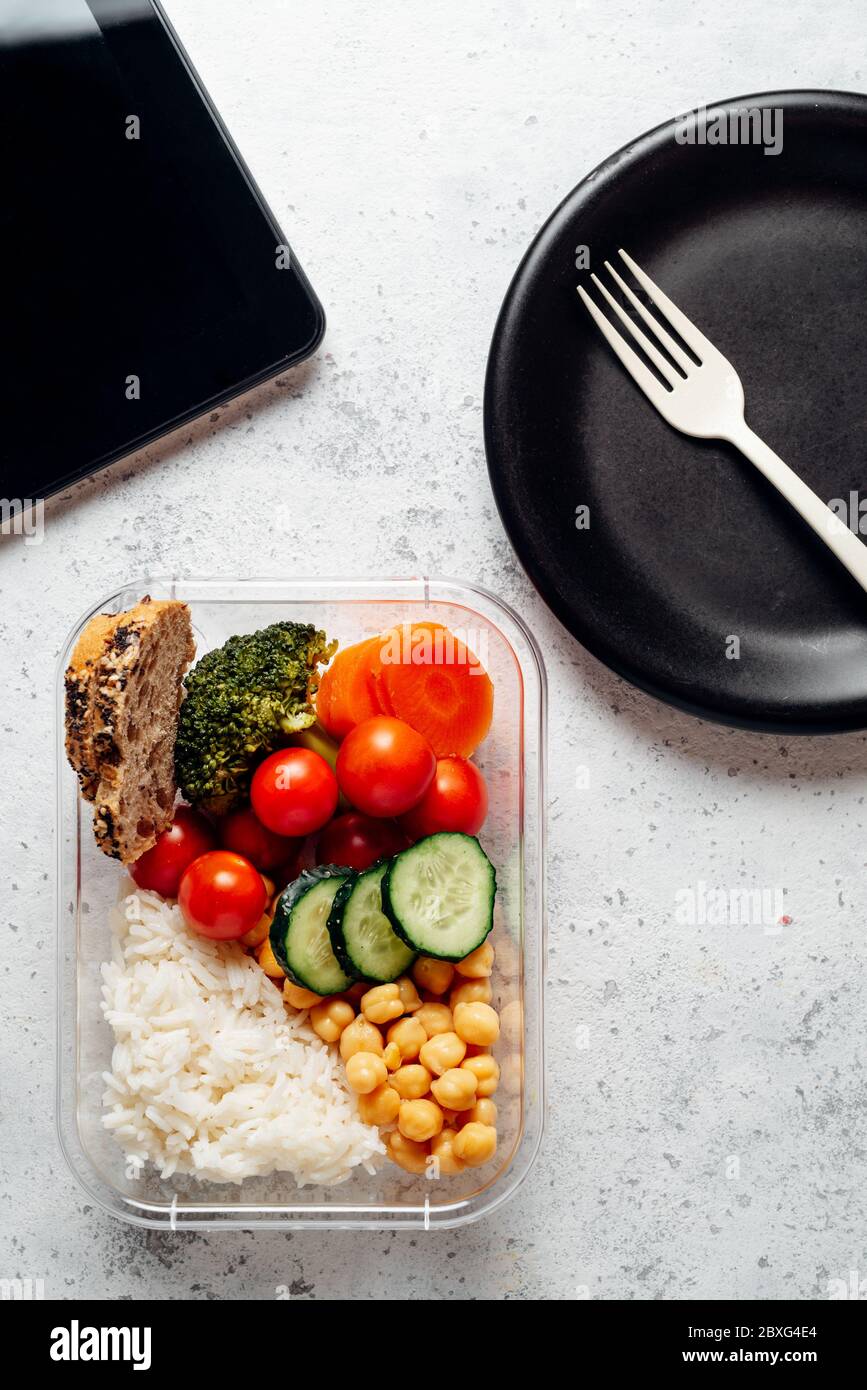 Healthy food in lunch box, on working table with the tablet. Basmati rice with chickpeas, broccoli, tomato and carrot, bread and fruit for dessert. ea Stock Photo