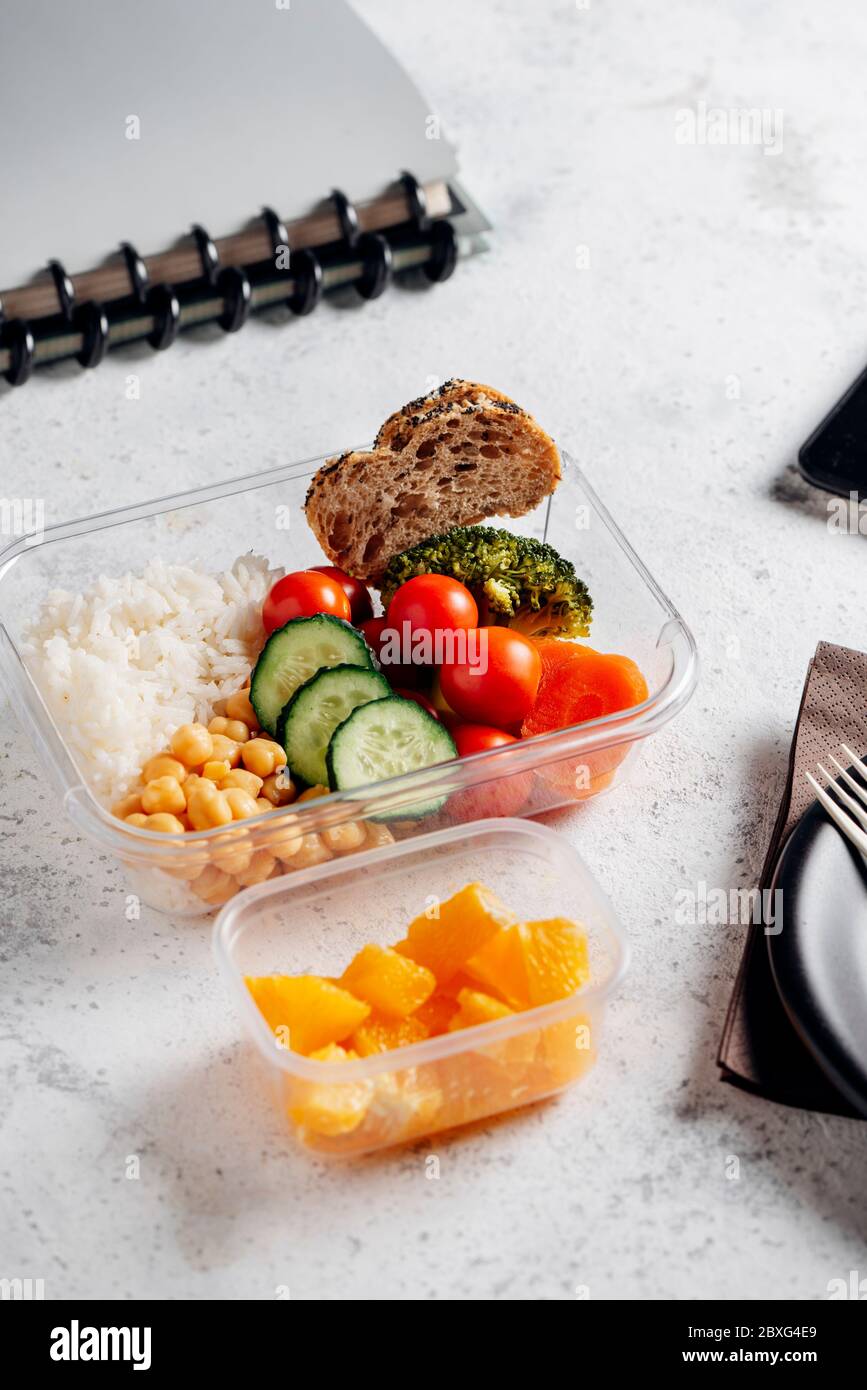 Healthy food in lunch box, on working table with the tablet. Basmati rice with chickpeas, broccoli, tomato and carrot, bread and fruit for dessert. ea Stock Photo