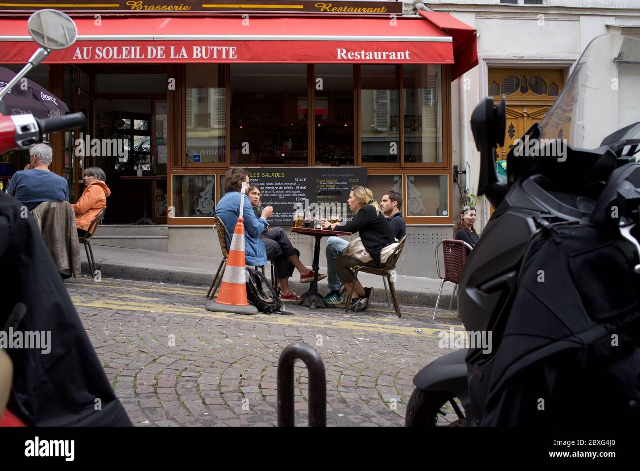 People enjoy a drink at a temporary café terrace, in a parking space, in life after lockdown - Rue Muller, Montmartre, 75018 Paris, France Stock Photo