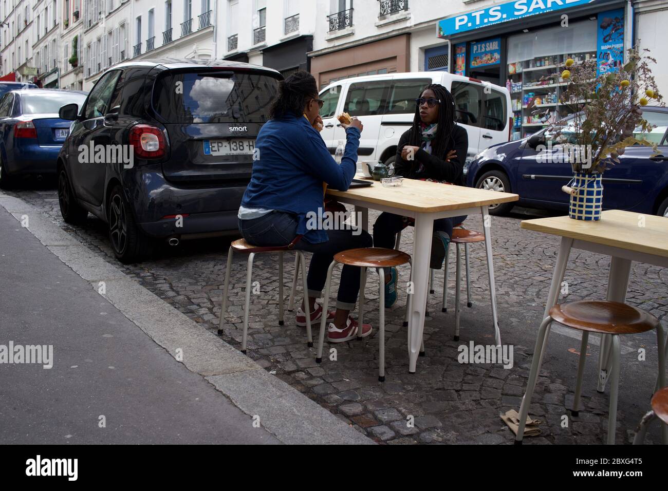 Parisians enjoy a temporary café terrace, between parked cars in life after lockdown - Rue Muller, Montmartre 75018 Paris, France Stock Photo