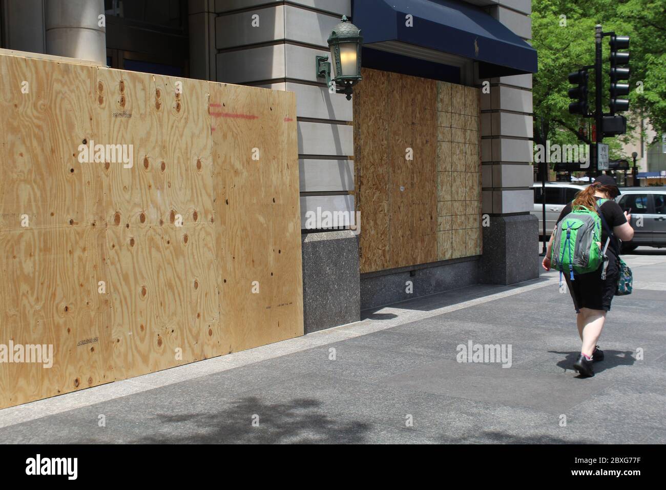 Woman with a backpack walking past a boarded up North Michigan Avenue store in Chicago after a riot Stock Photo