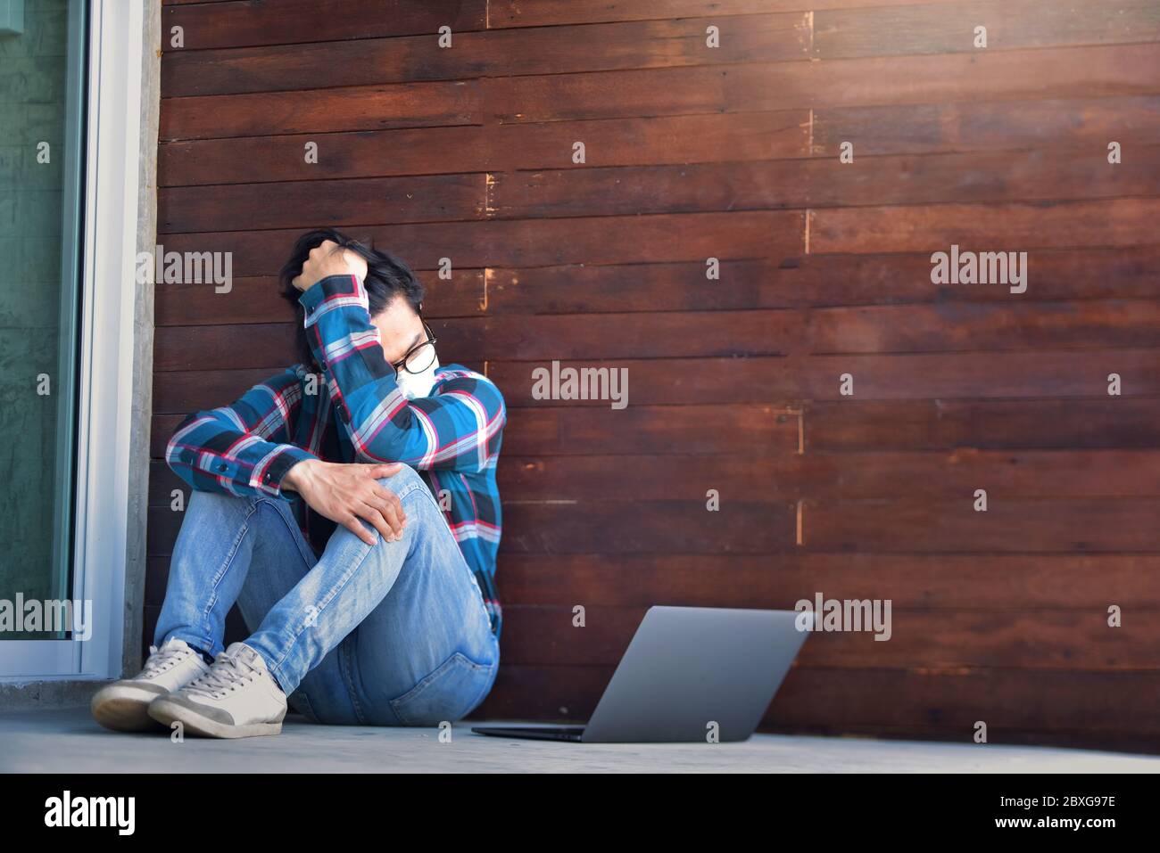Distressed man sitting on ground with his laptop during lockdown Stock Photo