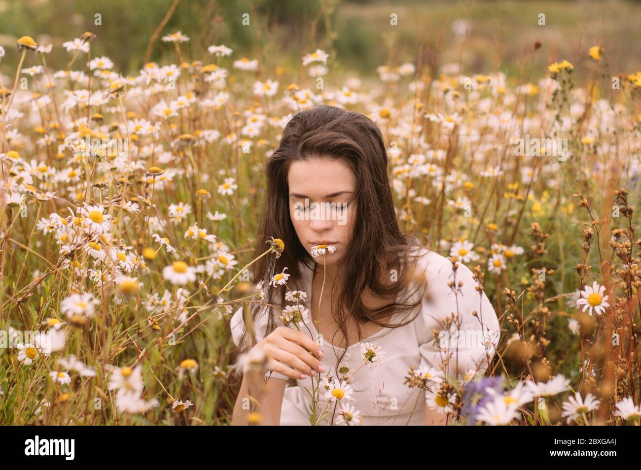 Young beautiful girl with closed eyes in white dress smelling flowers ...