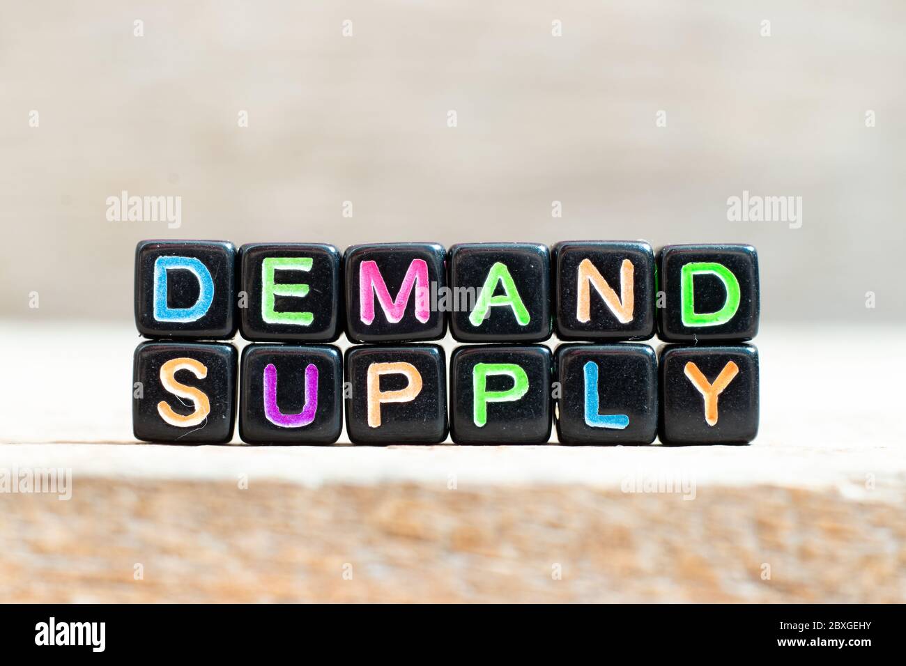 Black bead with color letter in word demand supply on wood background