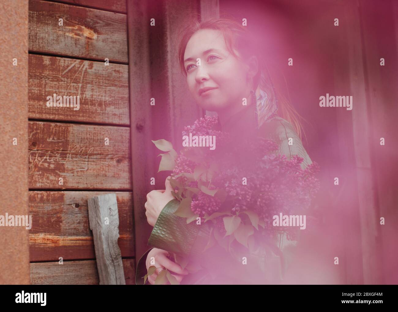 Portrait of a woman standing on a porch holding a bunch of flowers ...