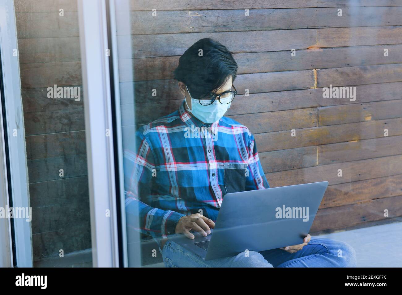 Man wearing a face mask sitting outdoors using a laptop, Thailand Stock Photo