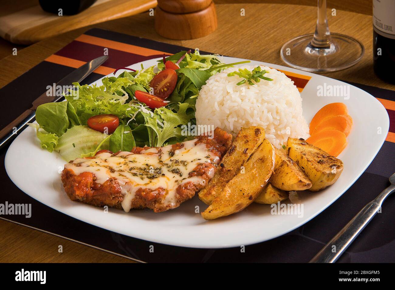 Breaded chicken with cheese, potato wedges, rice, lettuce, carrot and tomato salad Stock Photo