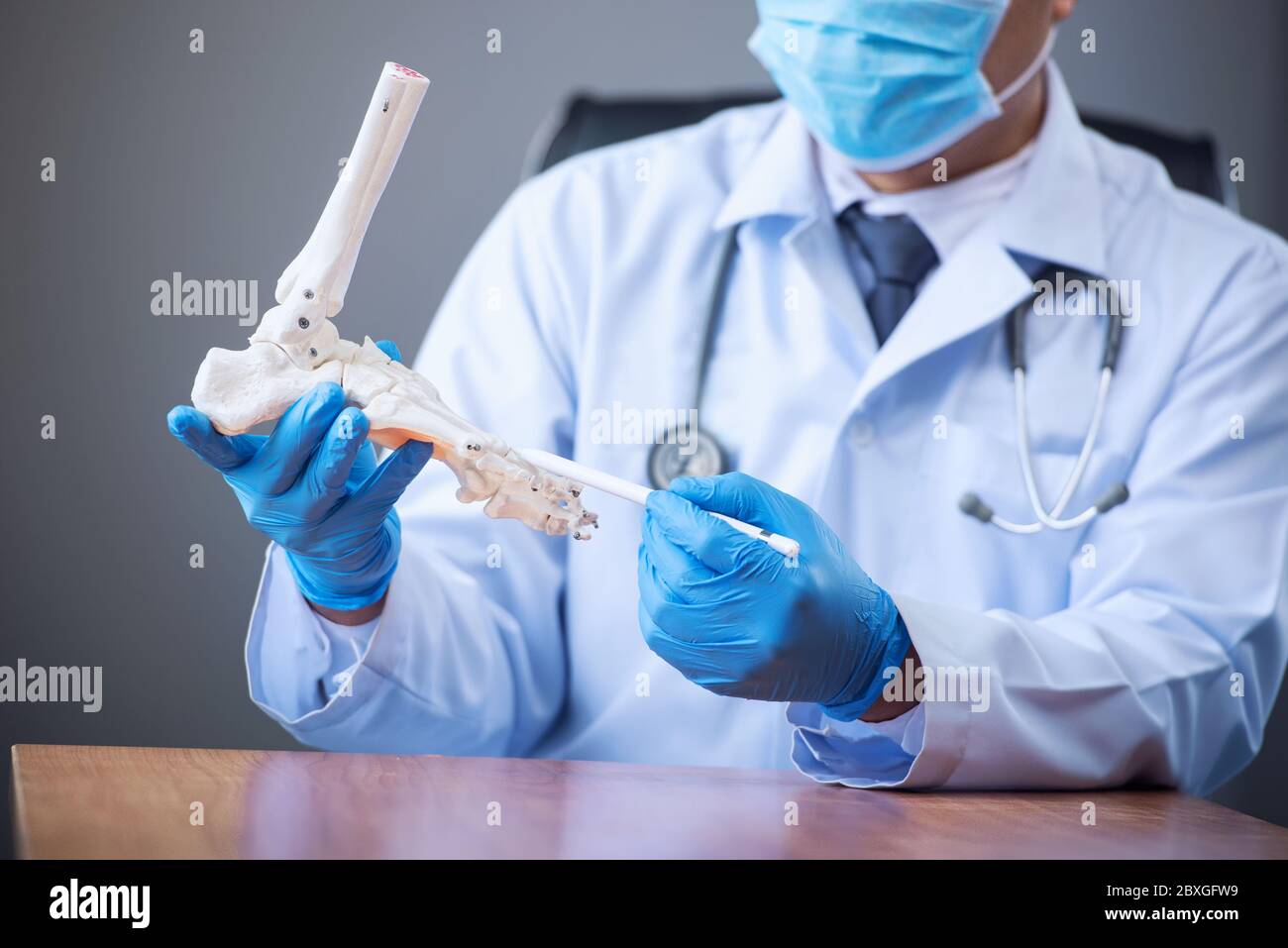 Doctor wearing a face mask holding a artificial foot bone Stock Photo