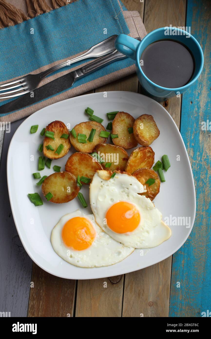 Fried eggs with roasted potato and green onion on a rustic table Stock Photo
