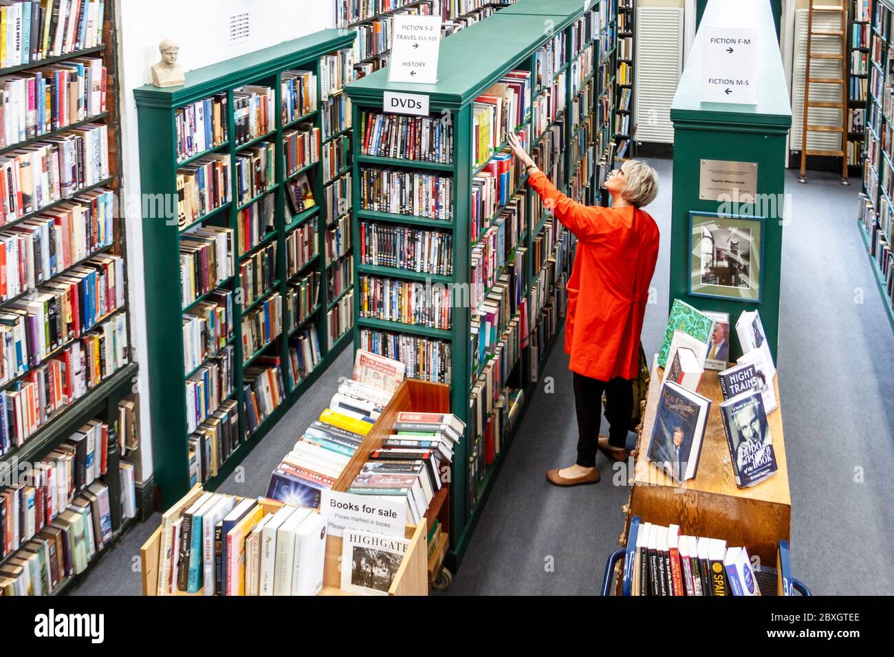 A woman in a red coat browsing the shelves of the HLSI library in Highgate Village, London, UK Stock Photo