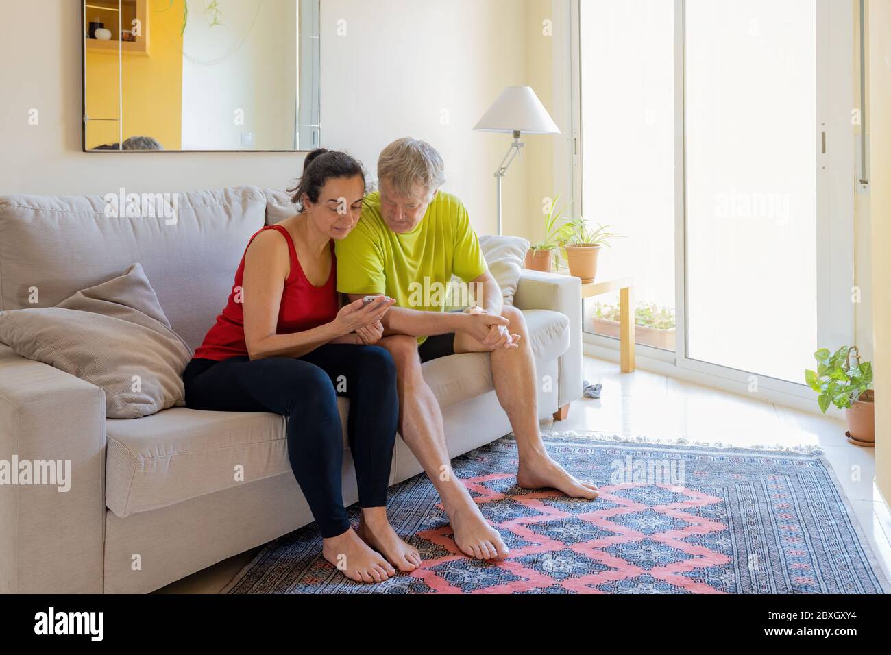 Middle-aged couple sitting on the sofa and communicating with cell phone Stock Photo