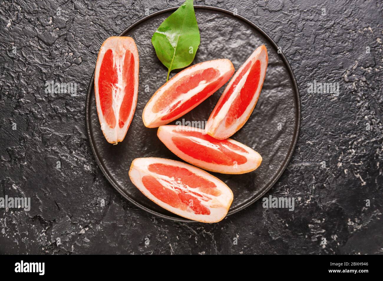 Plate with fresh sliced grapefruit on dark background Stock Photo