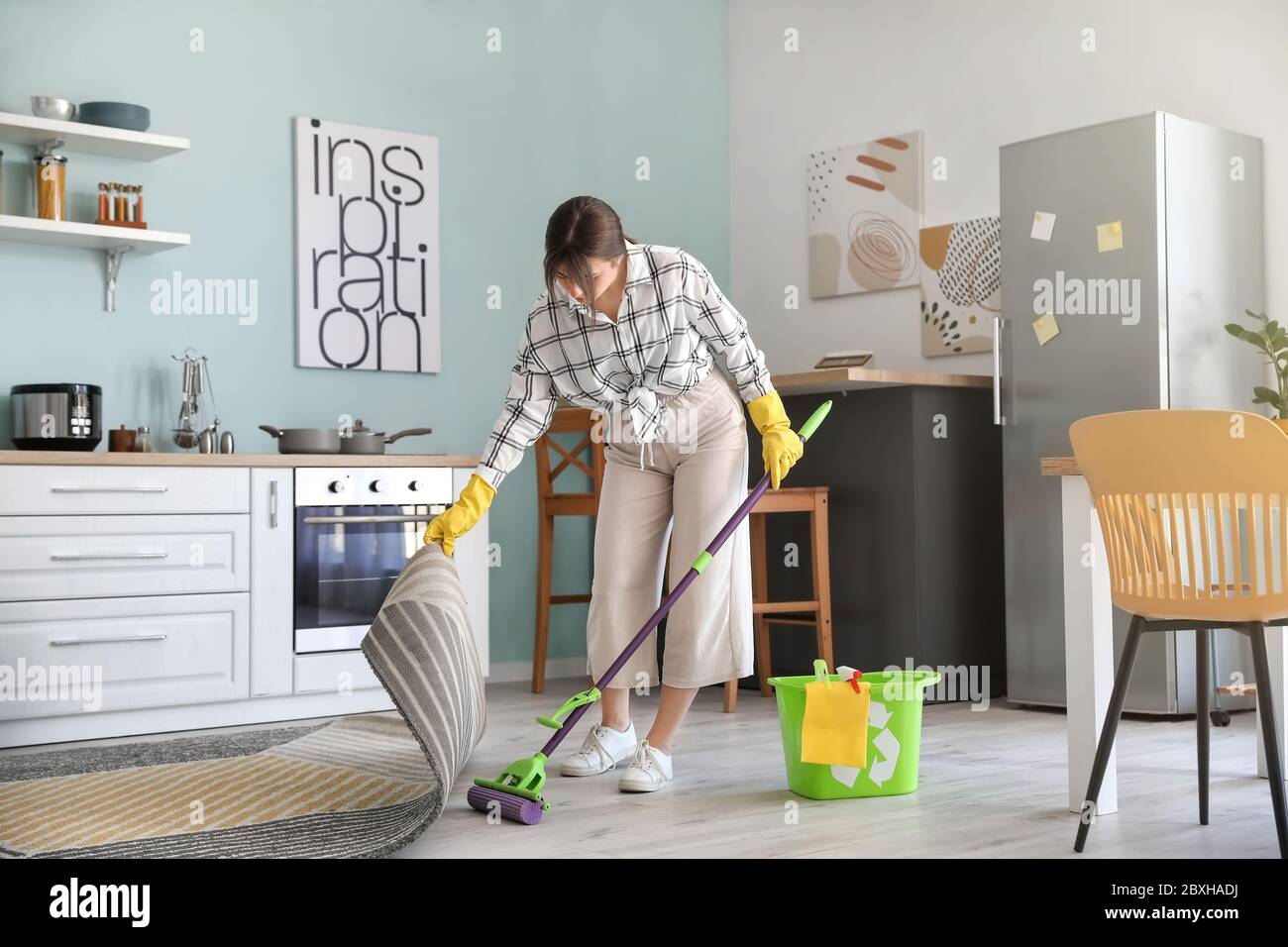 Young woman mopping floor in kitchen Stock Photo