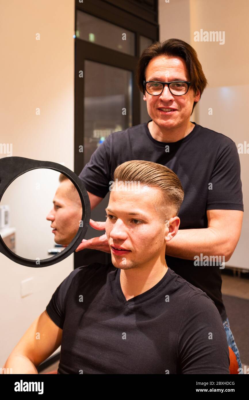 Hairdresser shows young man after cutting his hair with a mirror his