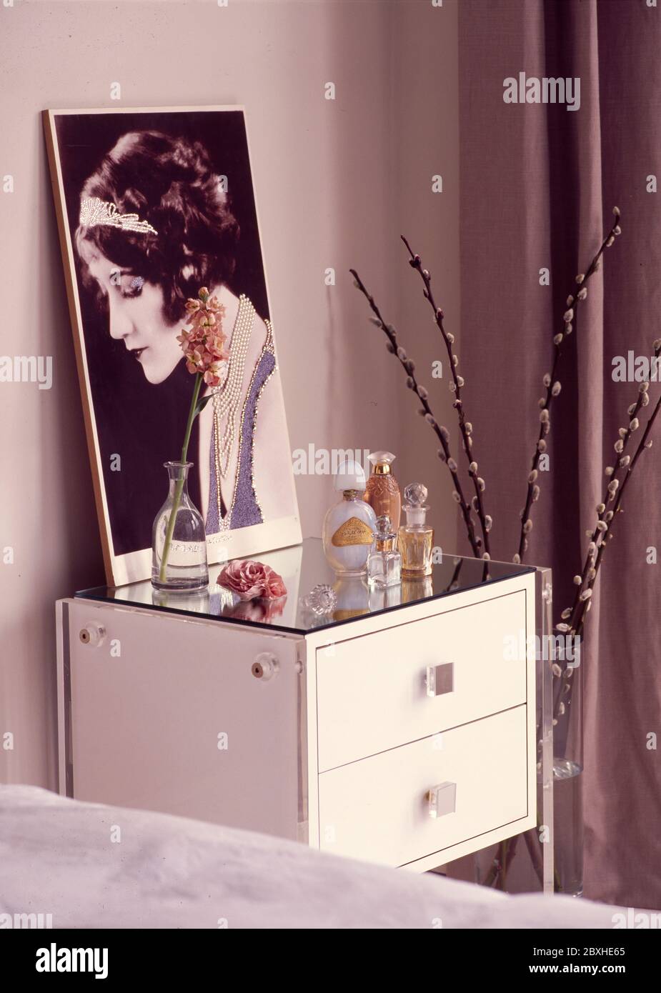 Bedside table with mirrored surface, large pramed photograph and collection of perfume bottles Stock Photo