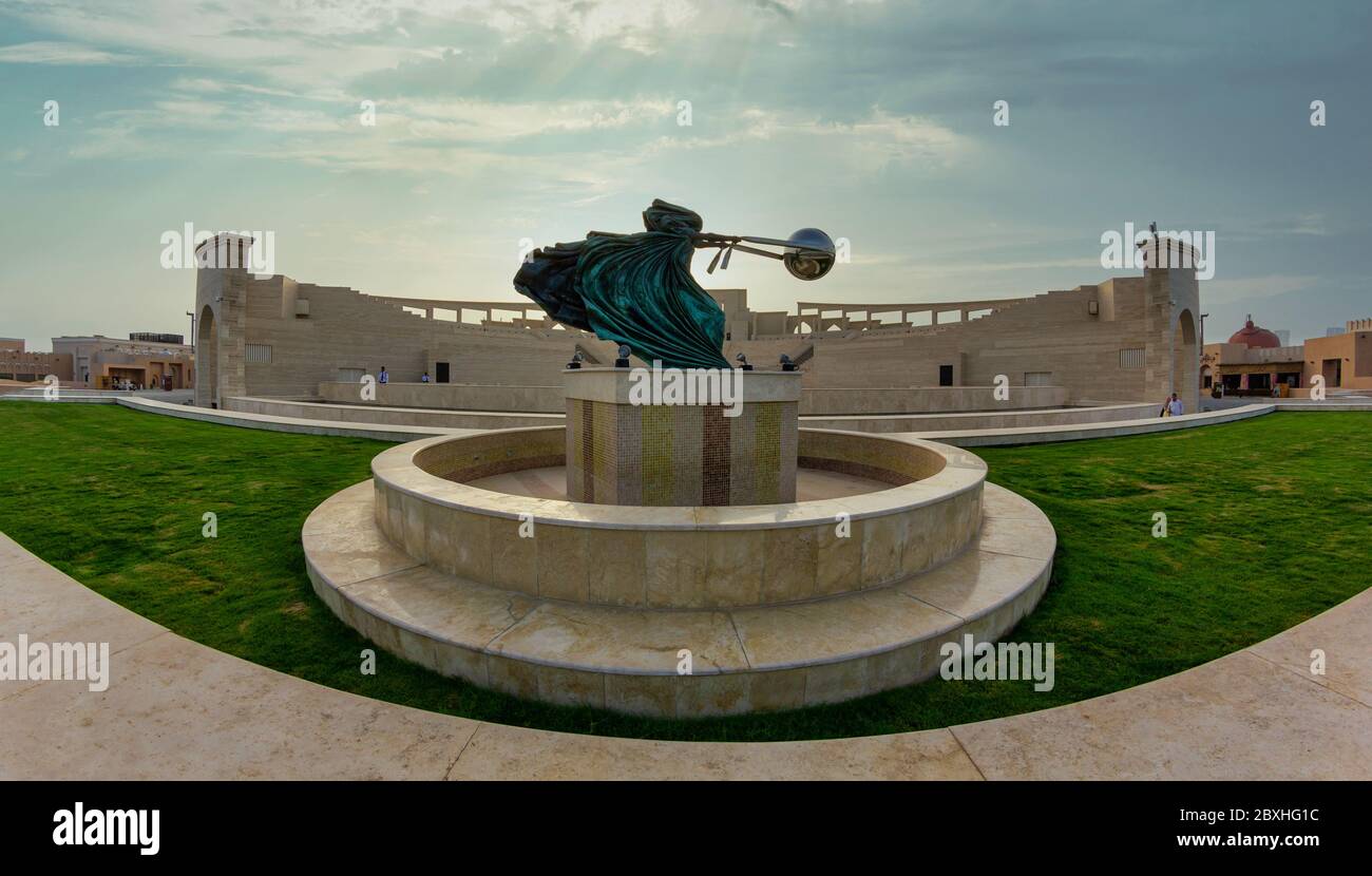 The amphitheater in Katara Cultural Village, Doha Qatar panoramic view in daylight  with Force of Nature 2 statue in foreground and clouds in the sky Stock Photo