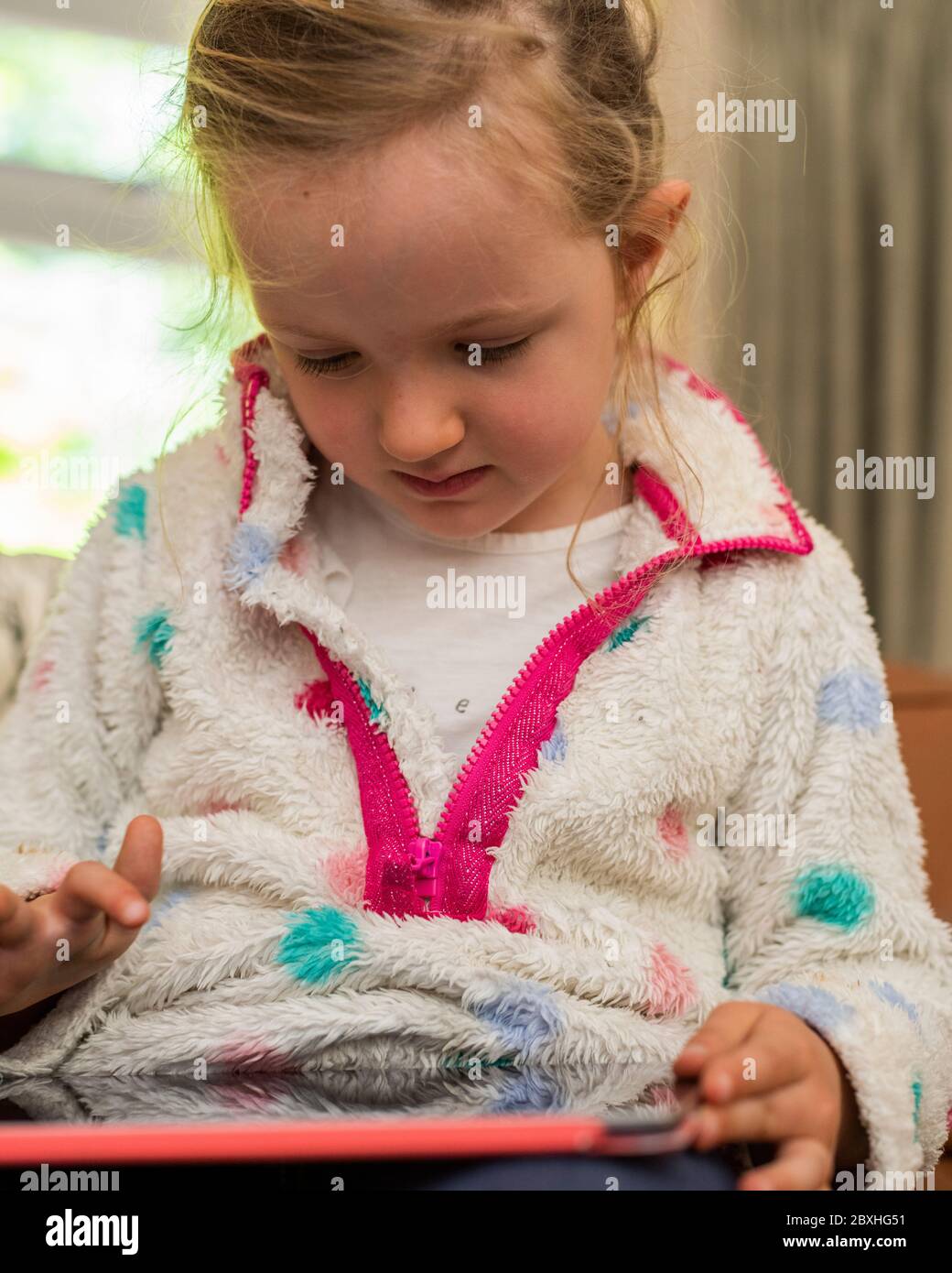 Pre-school girl looking at tablet, little girl playing with tablet, sitting on sofa playing with tablet, girl sitting on sofa playing on tablet Stock Photo