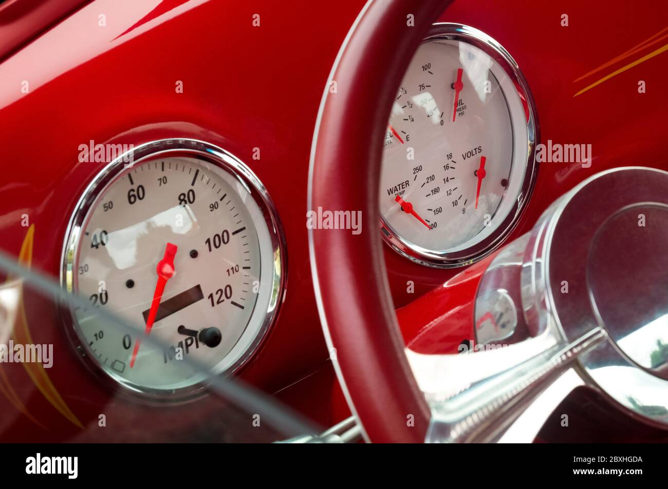 Steering wheel with crome beams, speedometer, fuel, oil, water, volts dials on front panel of red old timer car Stock Photo