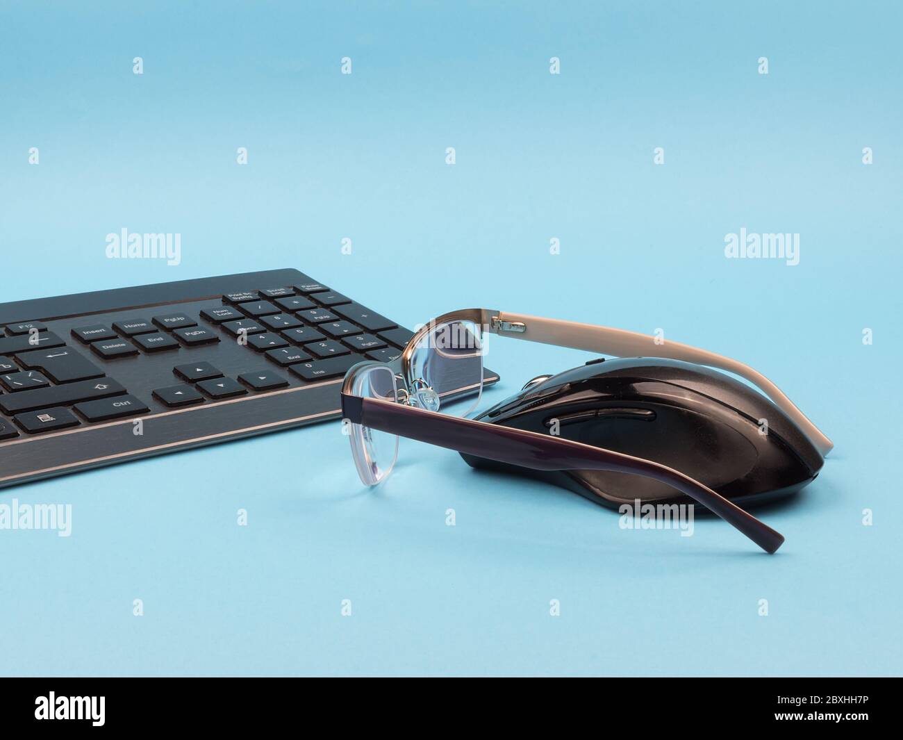 Keyboard, mouse and glasses on a blue background. Stock Photo
