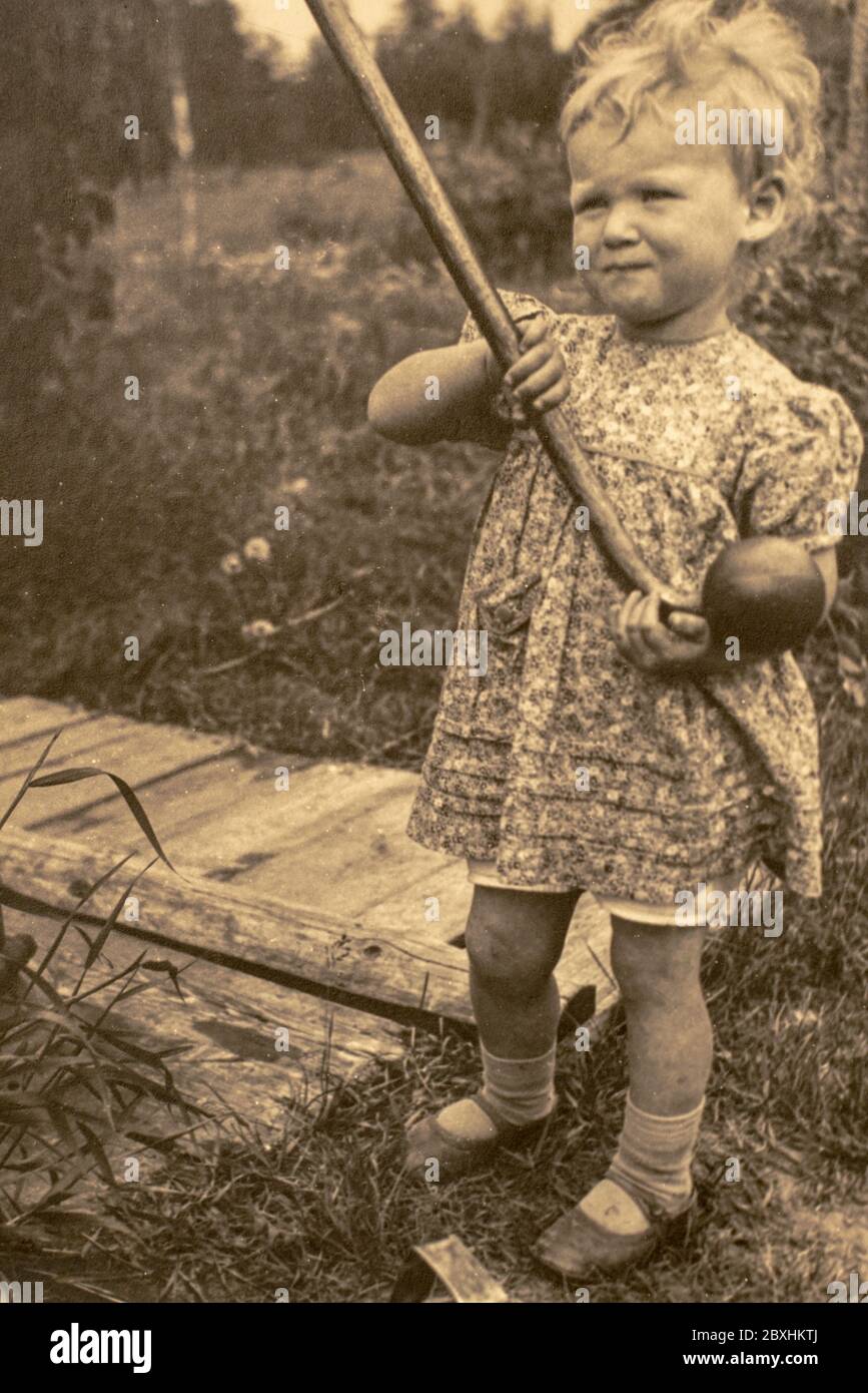 Latvia - CIRCA 1930s: Portrait of girl at hand pump well in garden. Vintage archive Art Deco era photography Stock Photo