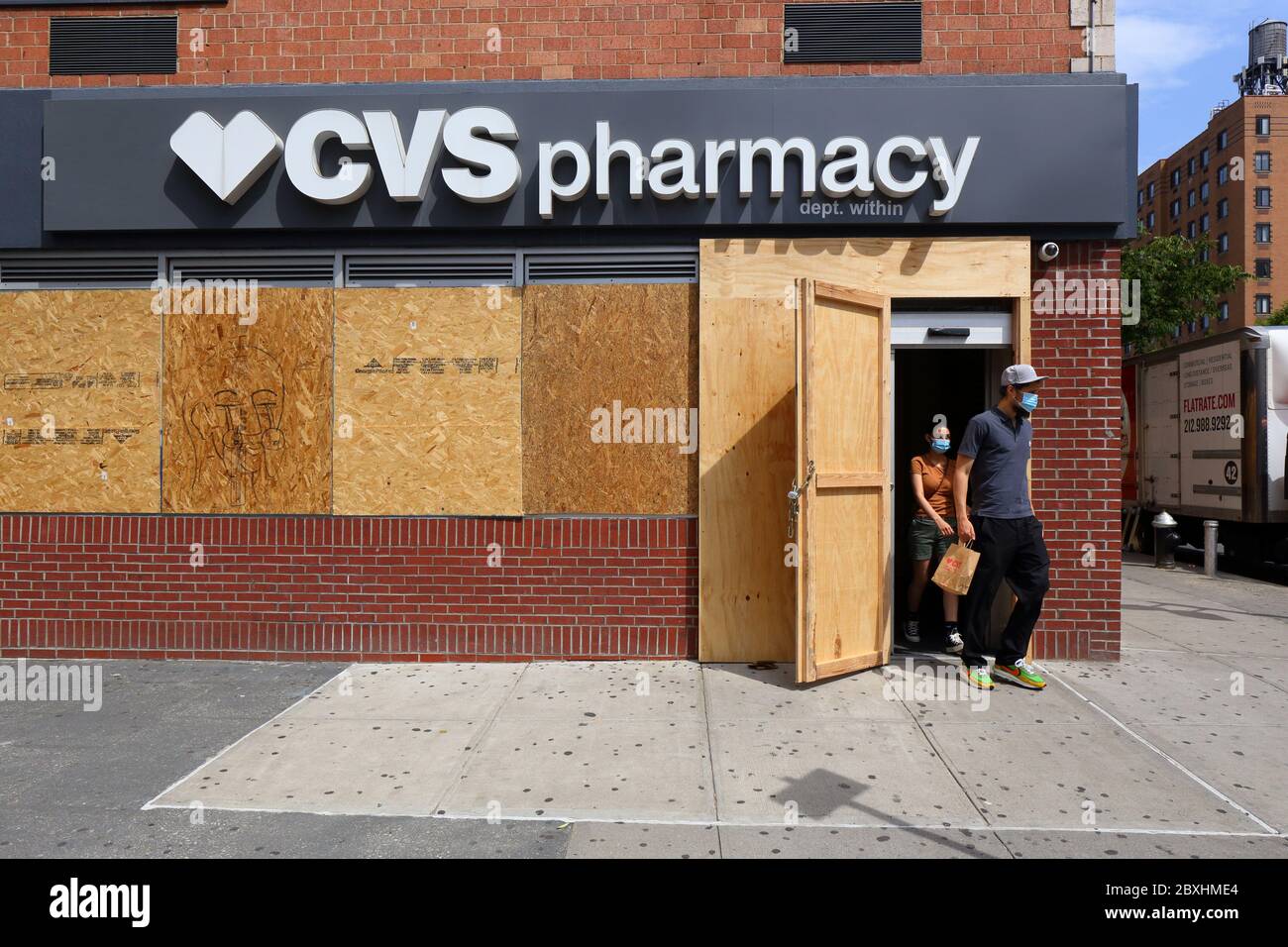 New York, NY. 4th June 2020. Shoppers exiting a CVS pharmacy with boarded up windows after a recent spate of large scale, organized burglaries/looting elsewhere in the city. The store joins other businesses across the city fearful of vandalism by boarding up their windows and doors as a precautionary measure while staying open for business during the covid 19 pandemic. The many shuttered storefronts across the city sends a message of hopelessness and despair to many not used to seeing so many shuttered storefronts in a normally vibrant and busy City. June 4, 2020 Stock Photo
